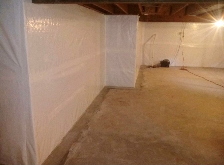 A clean, empty basement with white plastic wall coverings and exposed wooden beams. A single light bulb emits a warm glow, creating a tidy atmosphere.